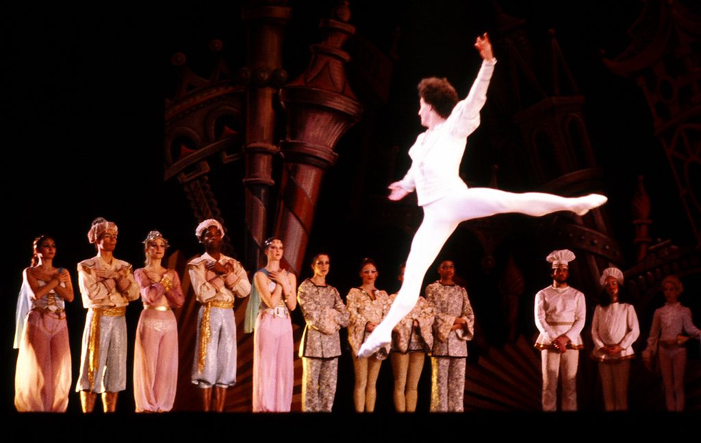 Un ballerino in bianco a mezz'aria in un grand jeté davanti agli altri interpreti