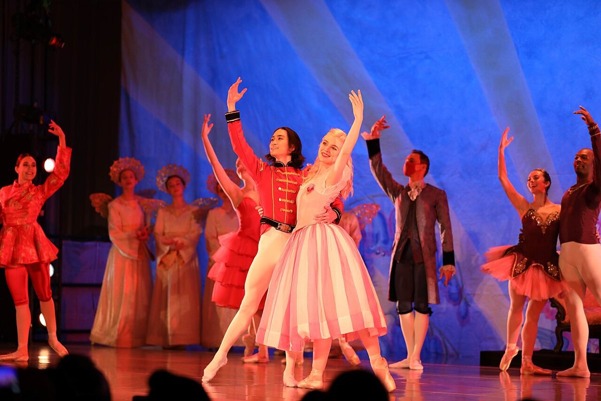 Lo Schiaccianoci in giubba rossa e Clara in tutù rosa al centro del palco, circondati dal corpo di ballo